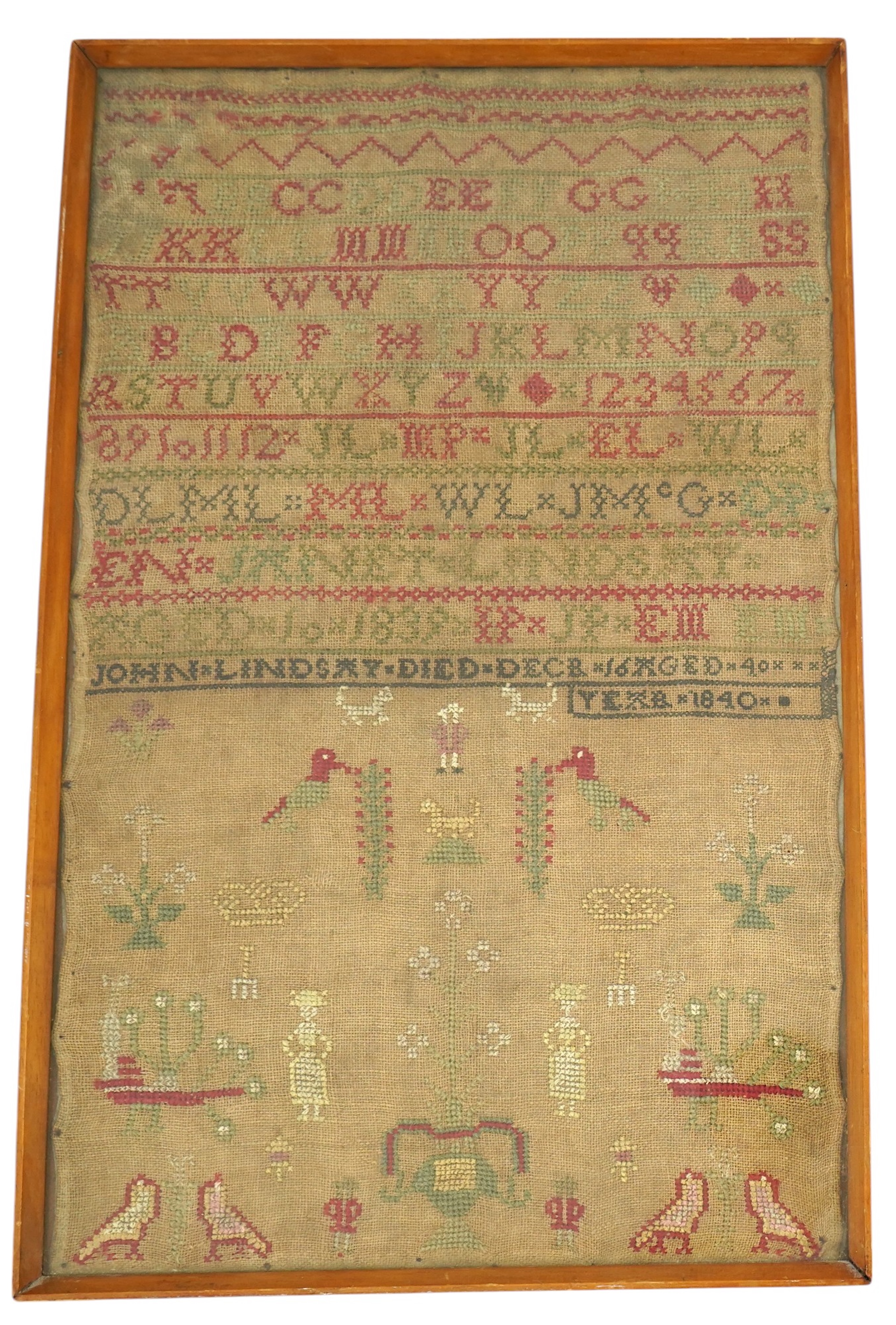 An alphabet cross stitch sampler with a figurative lower spot motif panel and commemorative dedication to John Lindsay, died Dec 16 1840, 27cm wide x 43.5 cm high. Condition - some light staining to linen, the blue and g